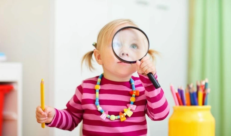 En liten flicka i rosarandig tröja tittar igenom ett förstoringsglas.
