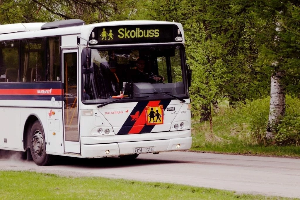 Skolbuss i Säters kommun från Dalatrafiken kör på en väg med grönska runtom.