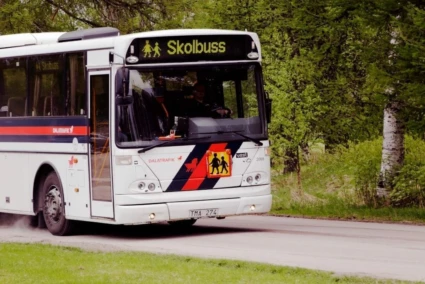 Skolbuss i Säters kommun från Dalatrafiken kör på en väg med grönska runtom.