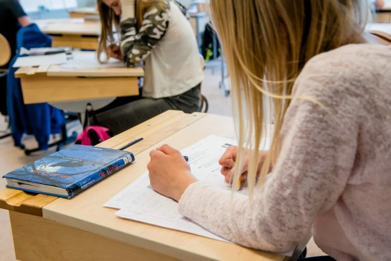 Skolelev sitter vid sin bänk och skriver.