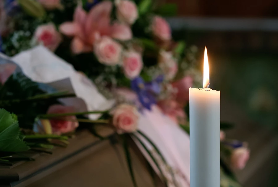 Ett ensamt stearinljus står och brinner framför en kista med blommor