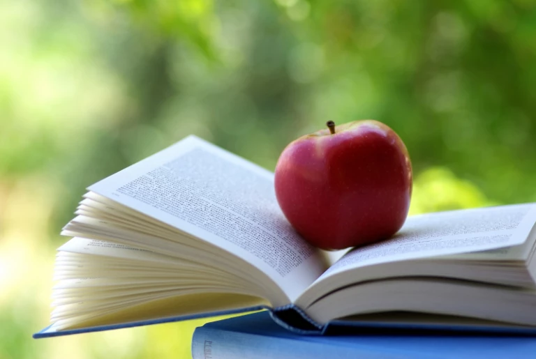 Ett rött äpple ligger ovanpå en uppslagen bok
