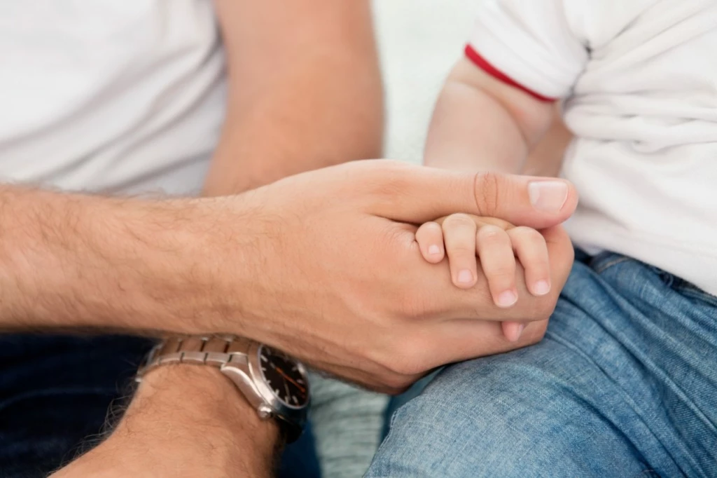 Close-up of father holding child's hand