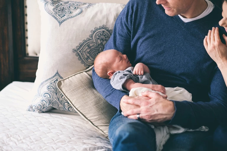 En man sitter i en soffa och håller i ett nyfött barn