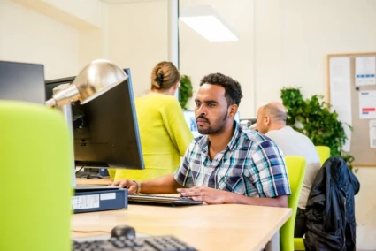 en man som sitter framför en dator vid ett skrivbord