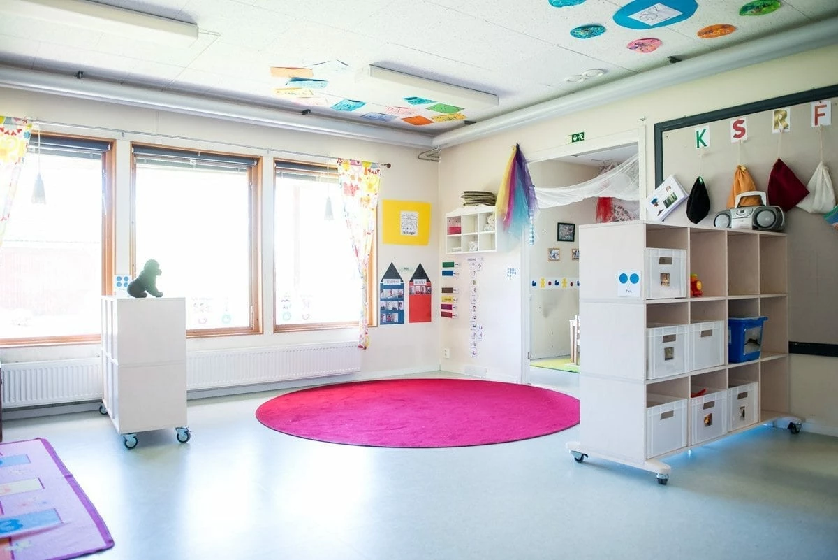 Kreativt lekrum med en rosa rund matta på golvet och hyllor med förvaring.