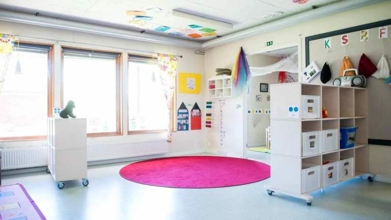 Kreativt lekrum med en rosa rund matta på golvet och hyllor med förvaring.