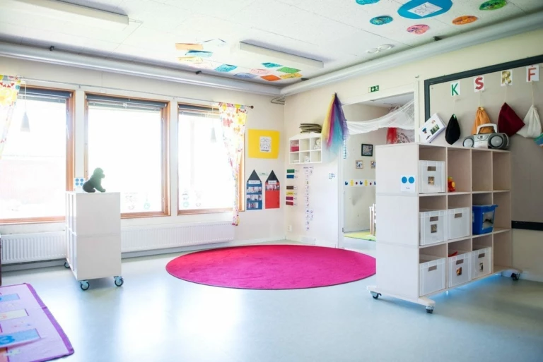 Kreativt lekrum med en rosa rund matta på golvet och hyllor med förvaring.