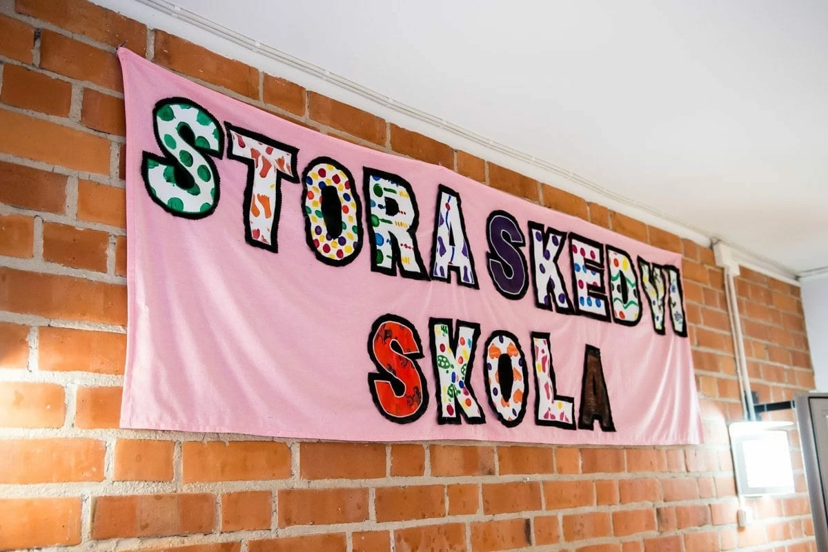 En banderoll med texten Stora Skedvi skola uppsatt mot en tegelväg inomhus.