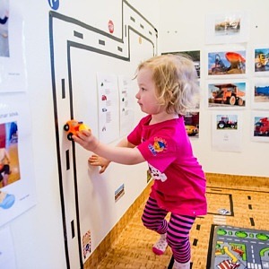 Ett litet barn kör med en leksaksbil uppför en vägbana på väggen.