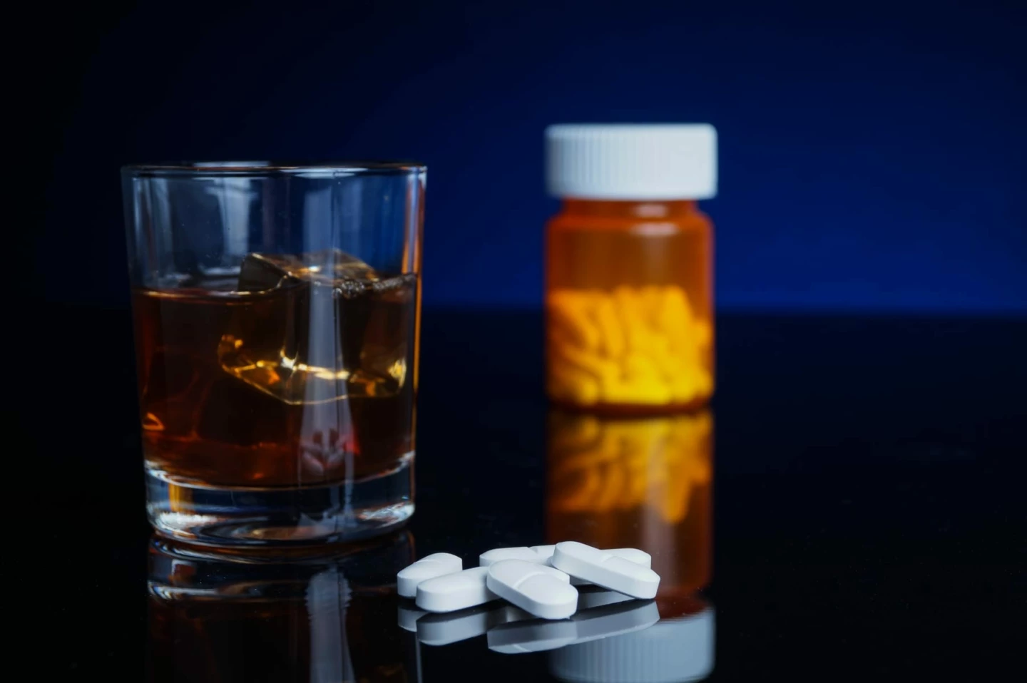 Ett glas med alkohol och en burk med tabletter står på ett bord