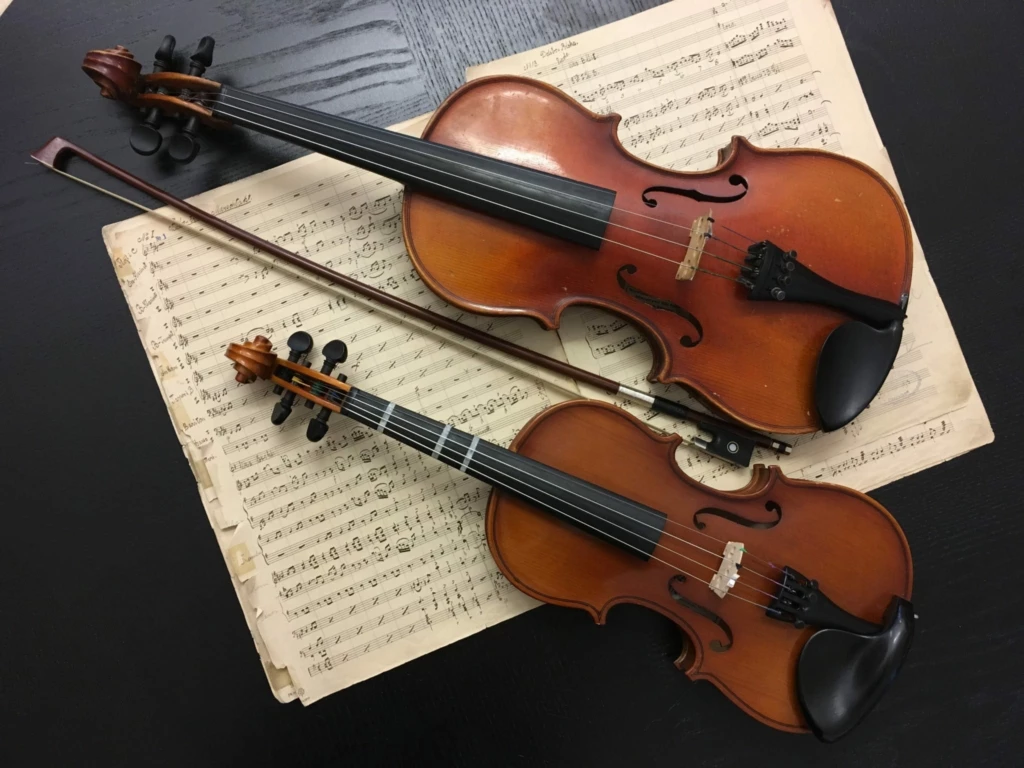 På ett svart bord ligger det notpapper och på noterna ligger även två stycken fioler.