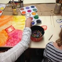 Två barn sitter och målar med vattenfärg vid ett bord.