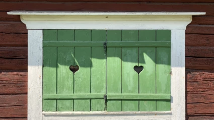 Gröna fönsterluckor på ett gammalt rött hus.