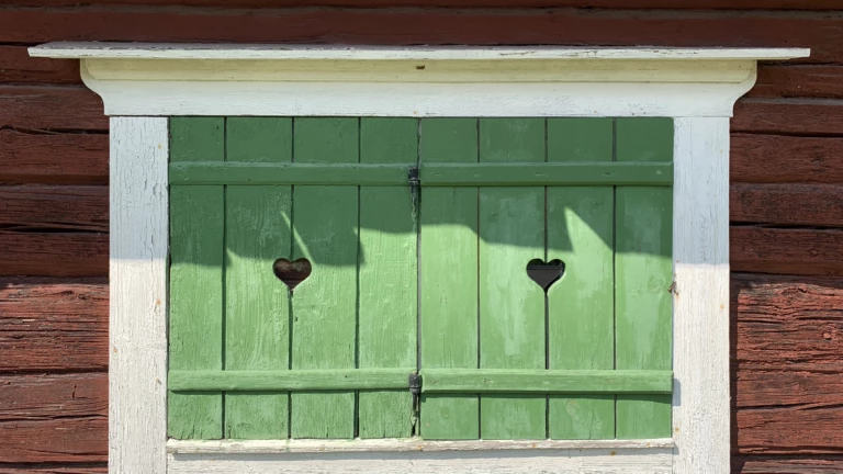 Gröna fönsterluckor på ett gammalt rött hus.