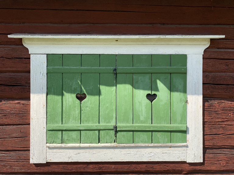Gröna fönsterluckor på ett gammalt rött hus.