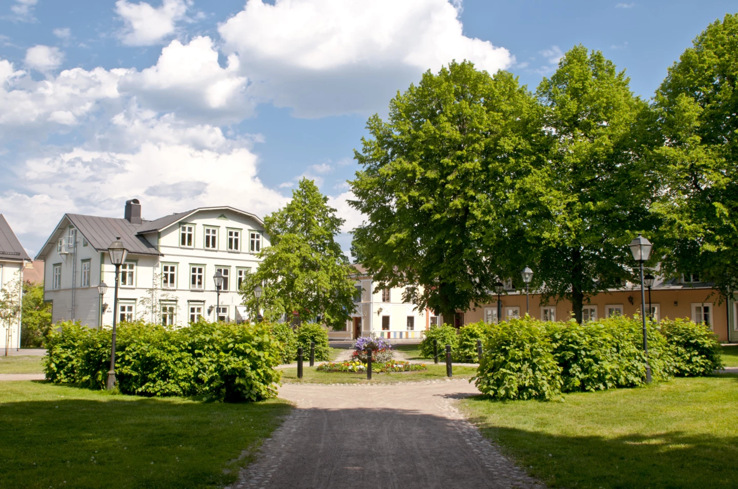 En grön lummig park i Säter vid ett gammalt vitt stenhus.