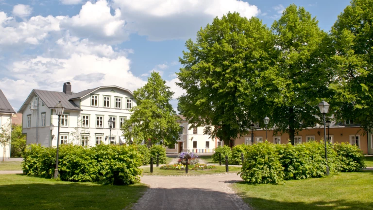 En grön lummig park i Säter vid ett gammalt vitt stenhus.