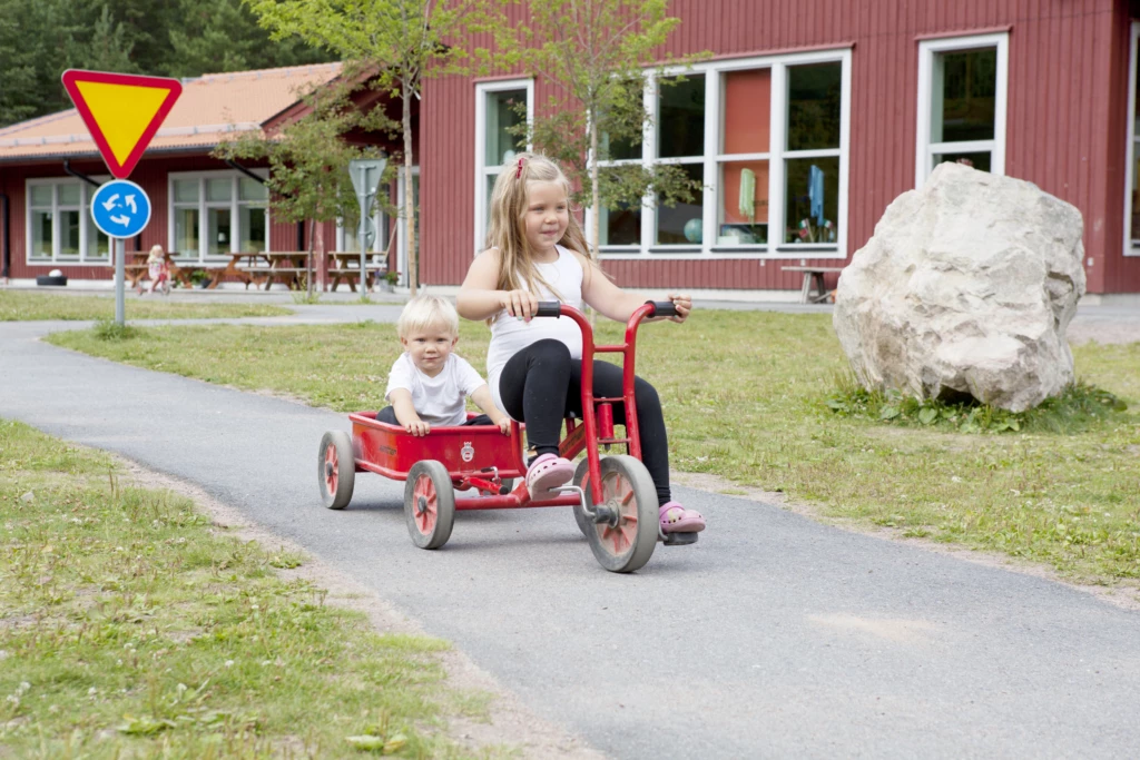 Två barn åker cykel på en förskolegård