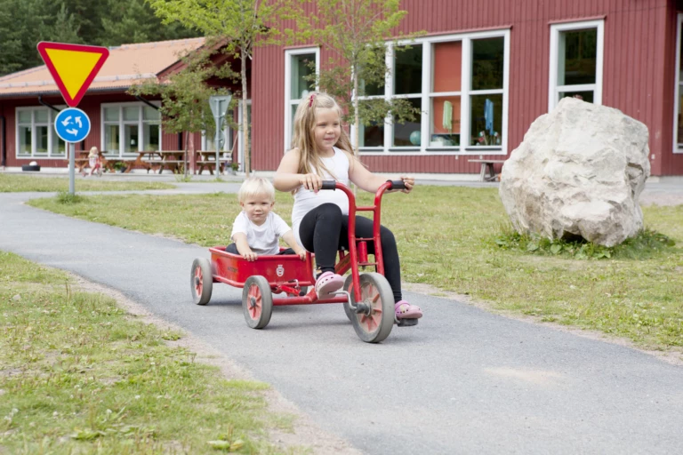 Två barn åker cykel på en förskolegård