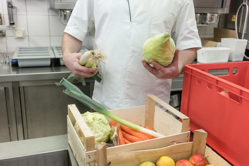 En person som håller i ett kålhuvud och några purjolökar