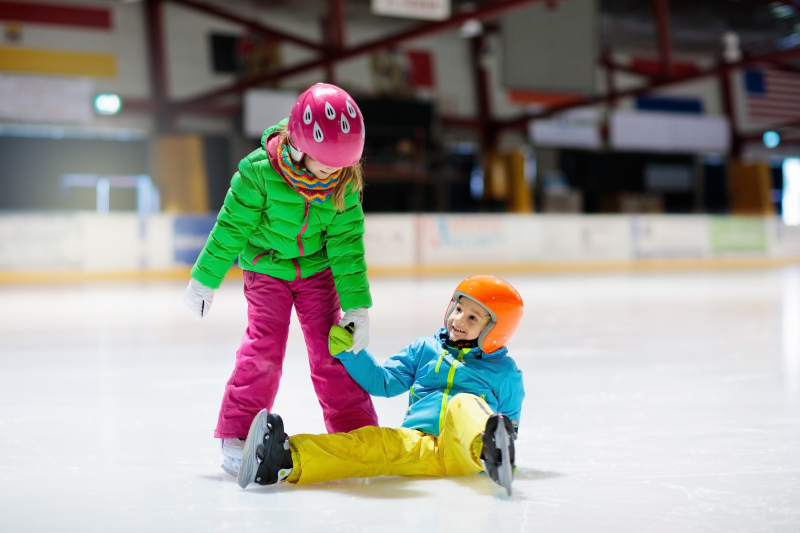 ett barn hjälper ett annat barn att ta sig upp från isen med skridskorna på