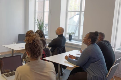 Skolklass med blandad etnicitet i klassrum lyssnar på läraren under vuxenutbildning / svenska för invandrare