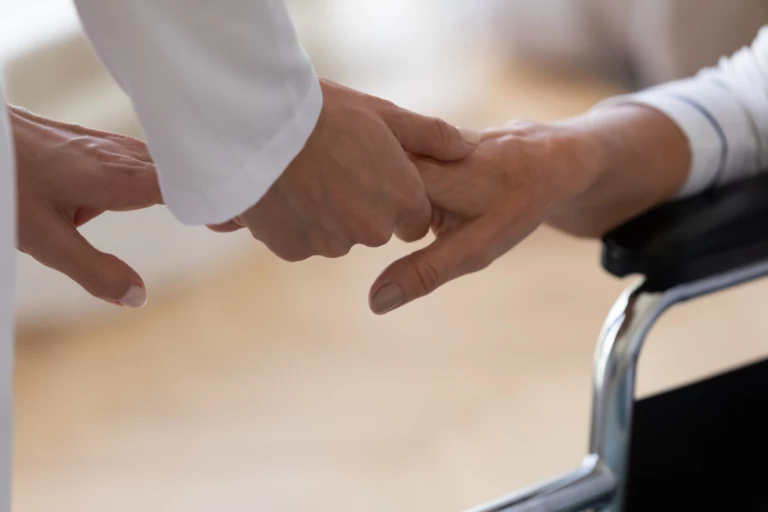 äldre person i rullstol håller handen med personal på särskilt boende.