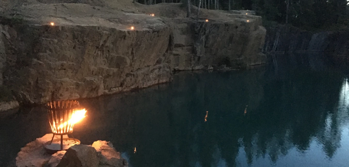 Naturbild över östra Silvbergs gruva i skymningen, Eldar brinner vid vattnet