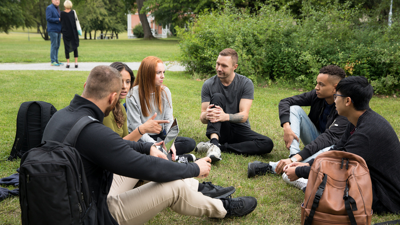 Några ungdomar sitter i en ring på gräset utanför campus.