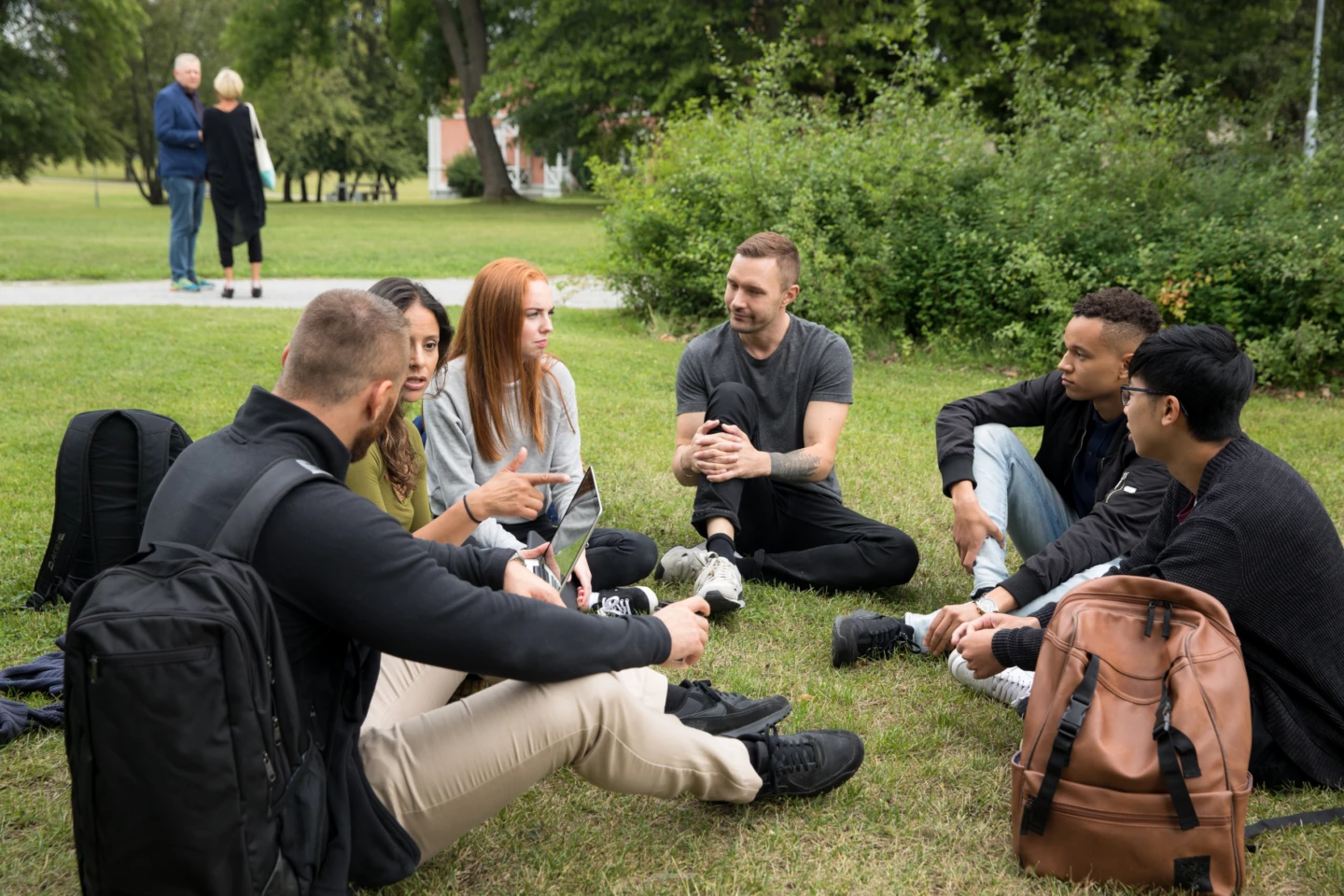 Några ungdomar sitter i en ring på gräset utanför campus.