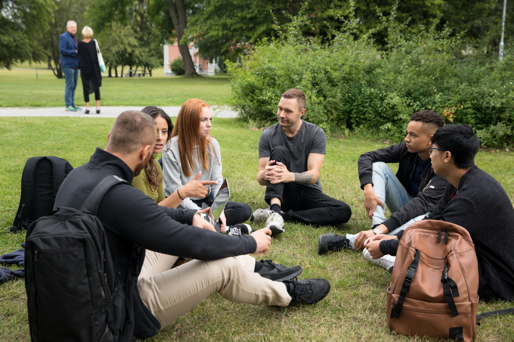 Några ungdomar sitter i en ring på gräset utanför campus.