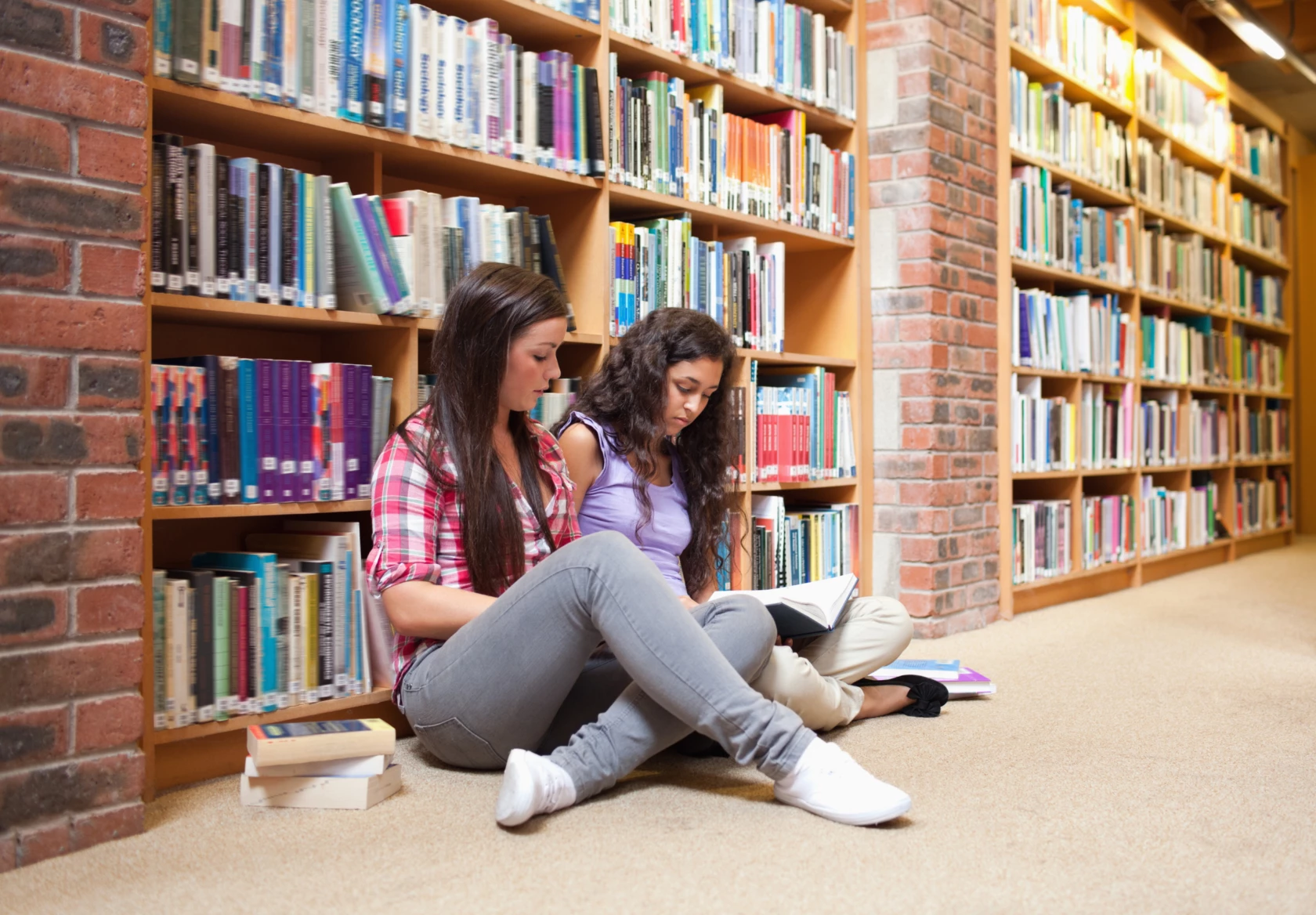 Två studenter sitter på golvet i biblioteket och studerar.