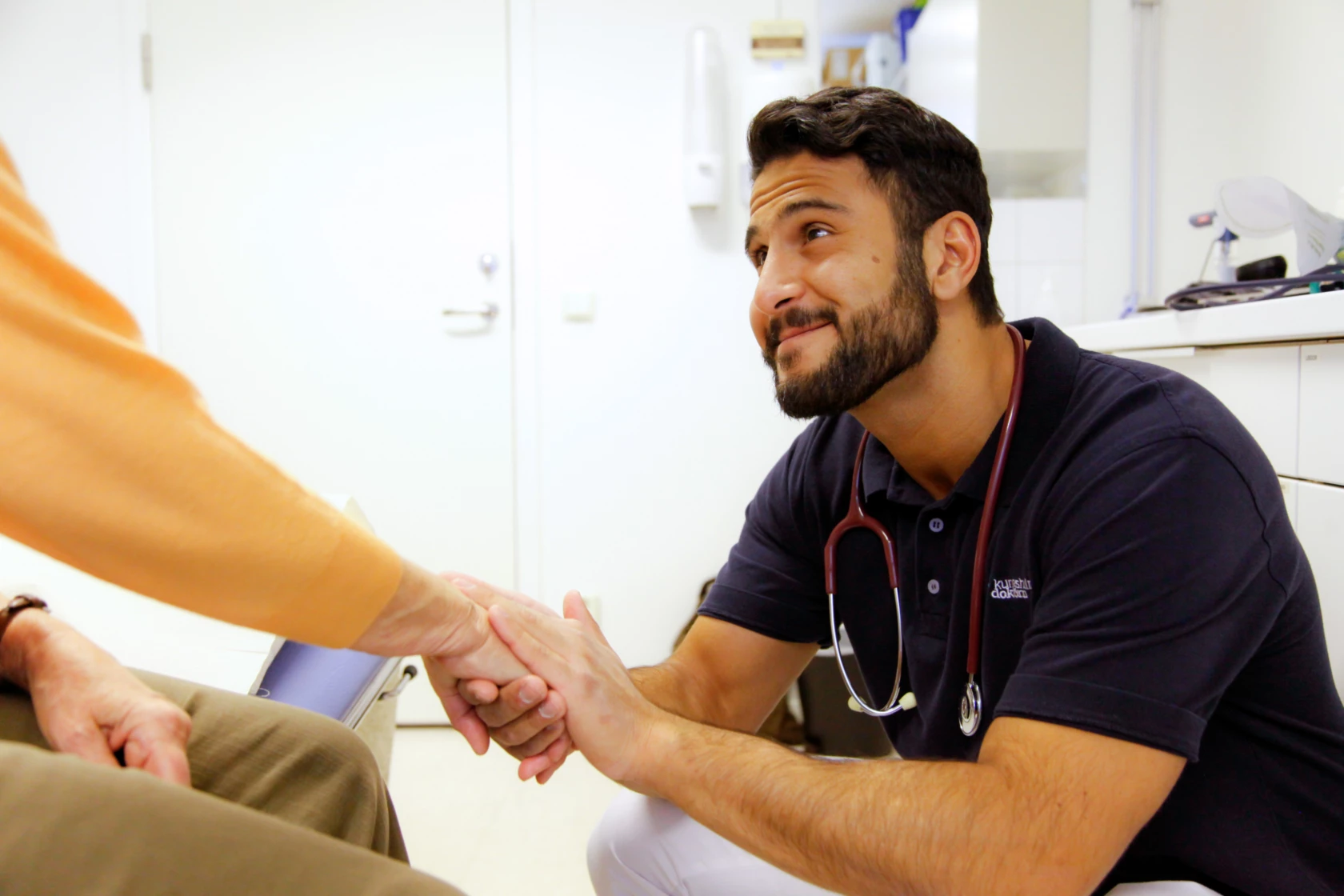 En manlig läkare tar patienten i hand vid ett vårdbesök.