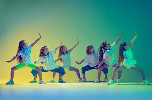 En grupp barn, små flickor i sportig casual stil kläder dansar i koreografi klass isolerad på grön bakgrund i neonljus. Begreppet musik, mode, konst.