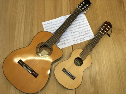 Två gitarrer ligger på golvet tillsammans med ett uppslag notblad. Den ena gitarren är stor och den andra är liten.