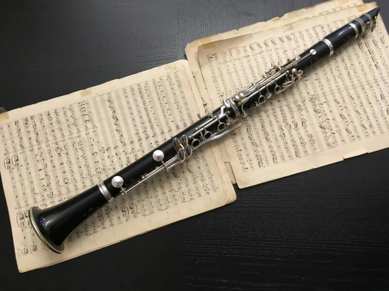 Klarinett som ligger ovanpå notblad på en svart bakgrund.