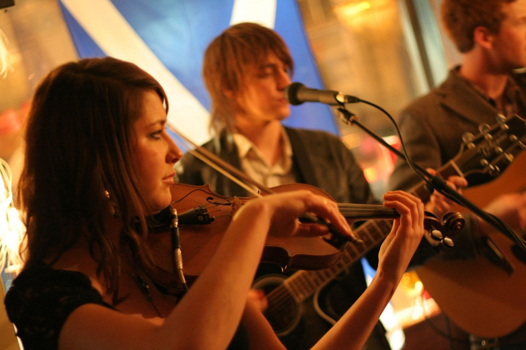 Här ser vi tre stycken elever som spelar i ett band. En flicka på fiol och två pojkar på gitarr.