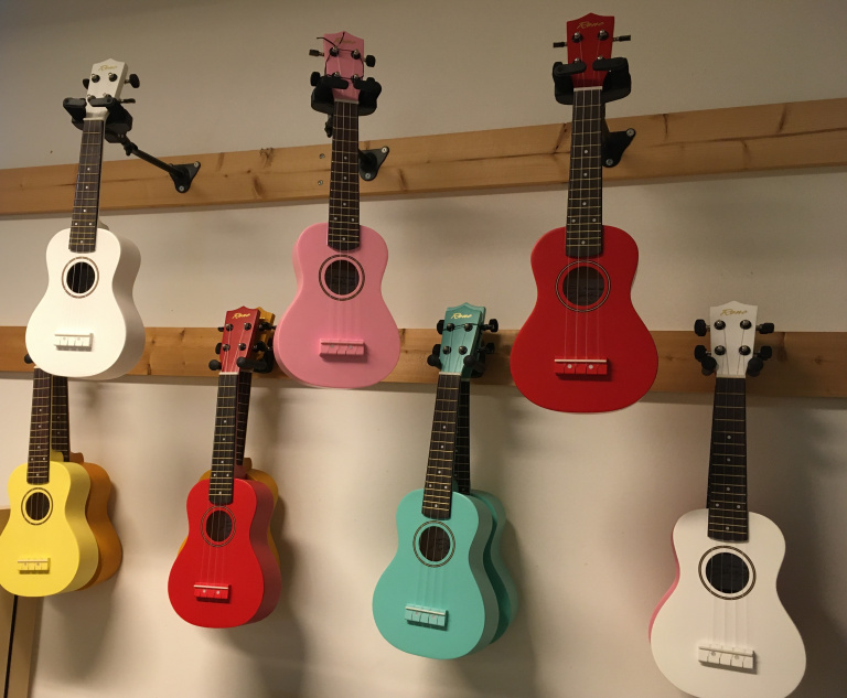 Här hänger sju stycken ukulele i olika färger på en vägg.
