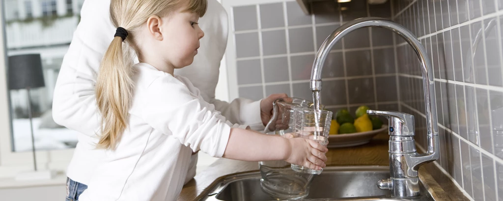 En flicka som häller vatten i ett glas från en kran