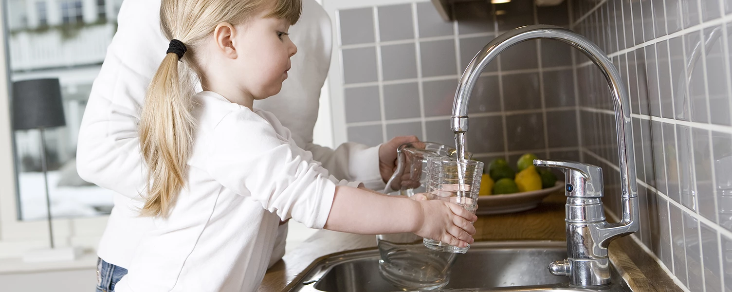 En flicka som häller vatten i ett glas från en kran