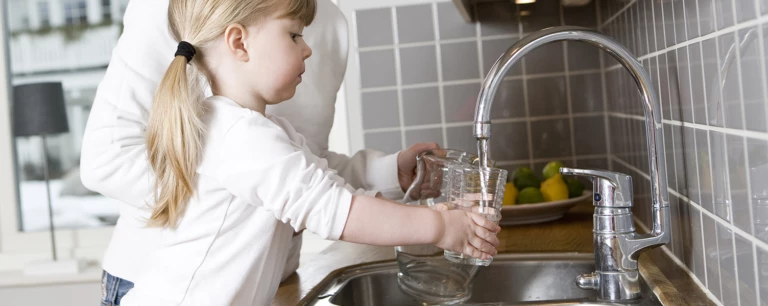 En flicka som häller vatten i ett glas från en kran