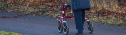 En äldre dam som är ute och går med en rollator