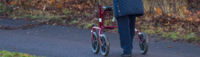 En äldre dam som är ute och går med en rollator