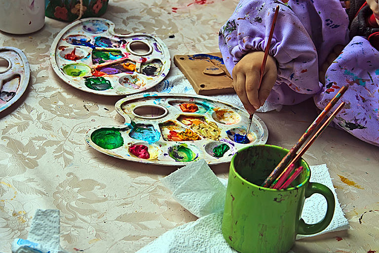 En bild på ett barns händer som målar med målarfärg med en pensel.