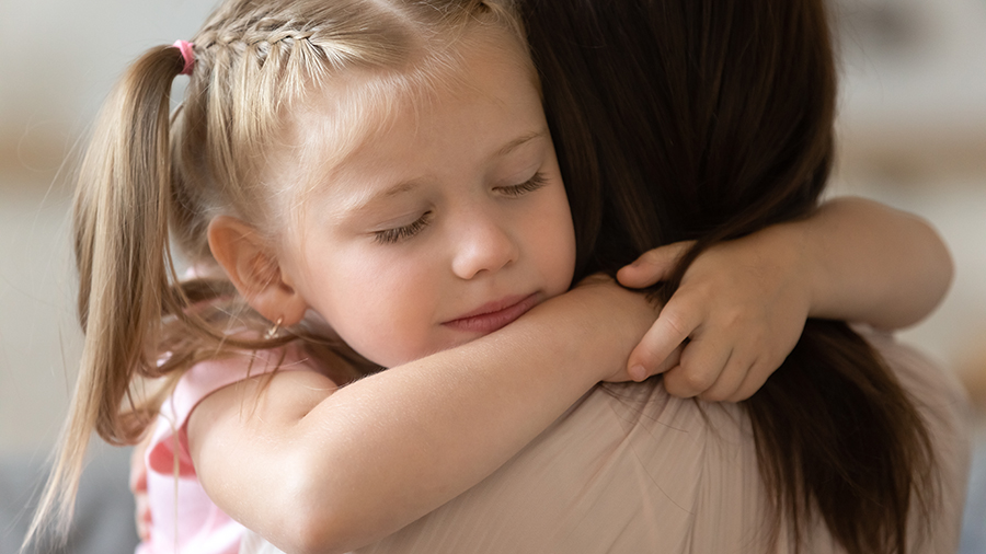 Närbild på en liten flicka som kramar sin mamma