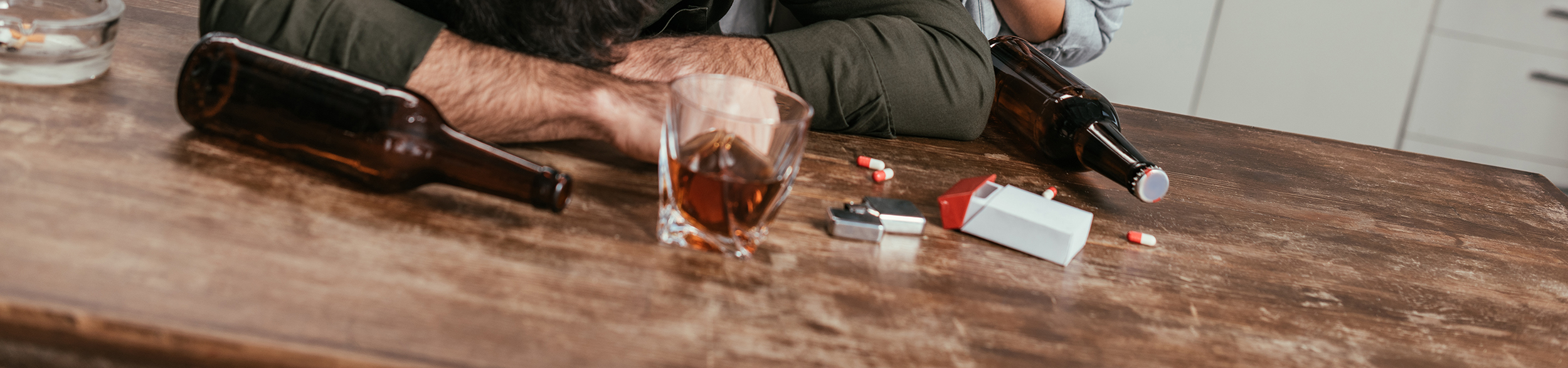 En man ligger vid ett bord där det ligger en flaska och tabletter