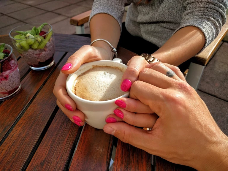 Två par händer som håller i varandra bredvid en kopp med kaffe på ett bord