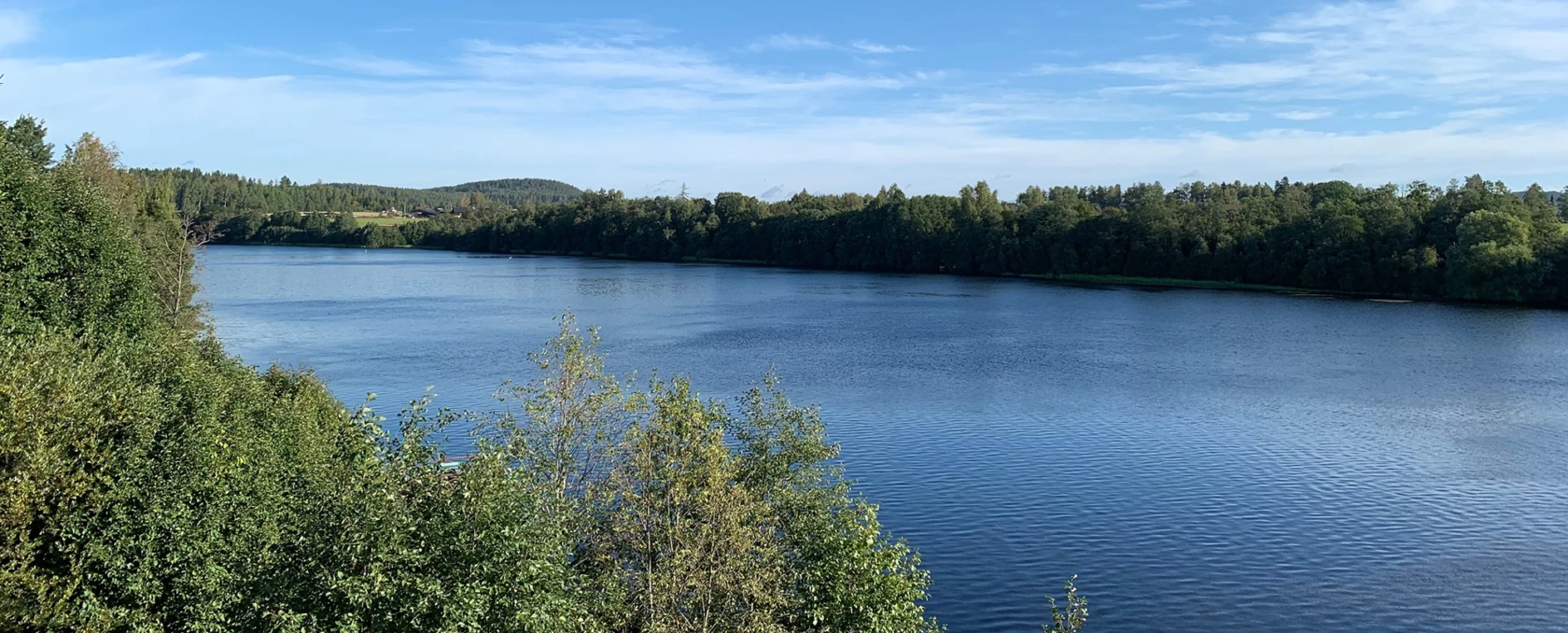 Vy över Dalälven med blått vatten, blå himmel och gröna träd
