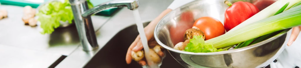 En kock på en restaurang sköljer grönsaker under rinnande vatten